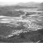 See how the camp site was a little above the level of the paddy fields that stretch to the distance across the valley. Across it runs the railway-the straight line-the winding Shum Chun River and Shung Shui lies toward the center. The border with China is just out of the picture to the left. The scenery is typical of the New Territories. The Guard Room is to the right, the tents the Battery occupied are either side of the track across the site, the officers tents up the valley to the left, and the cookhouse and NAAFI are toward the center in Nissen huts. The site is more compact than I recall.